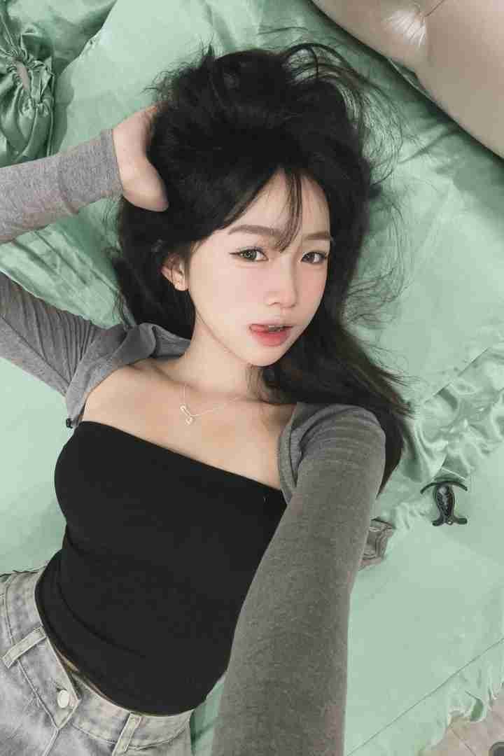 Malay Escort Girl Girl in black tube top lying on a green bed with messy hair and light makeup.