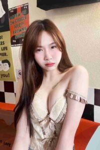 Malay Escort Girl Asian woman in a lacy top, posing near a cafe sign. Includes "Review us on Google, Free Brownie Cookie" text.