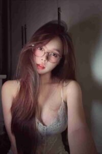 Malay Escort Girl Woman with glasses and long hair in a lace top, posing for a selfie.