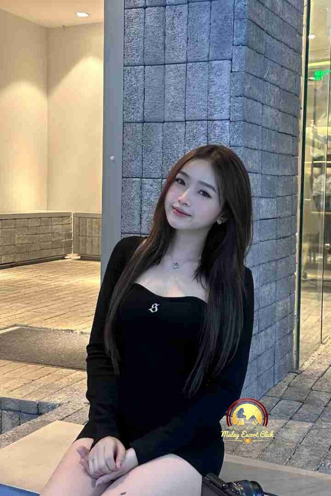 Smiling Asian woman in black dress sitting outside, long brown hair.