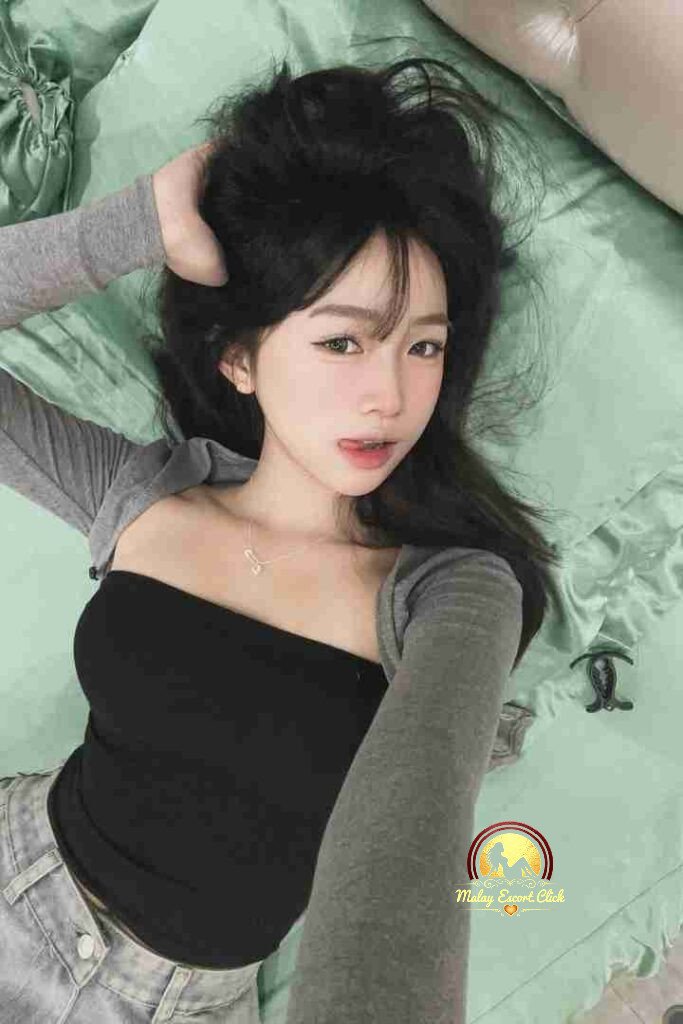 Asian woman lying on bed in black tube top and grey shrug, looking at camera.