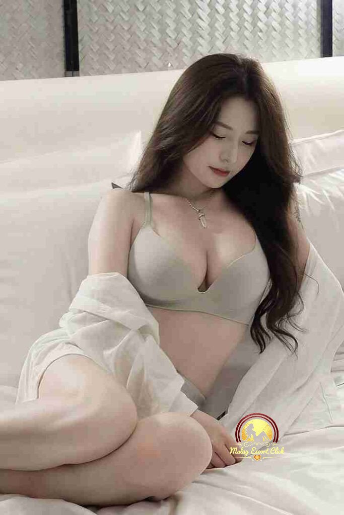 Beautiful Asian woman in bra and shirt on bed. Elegant, relaxed pose. Kuala Lumpur outcall escort.