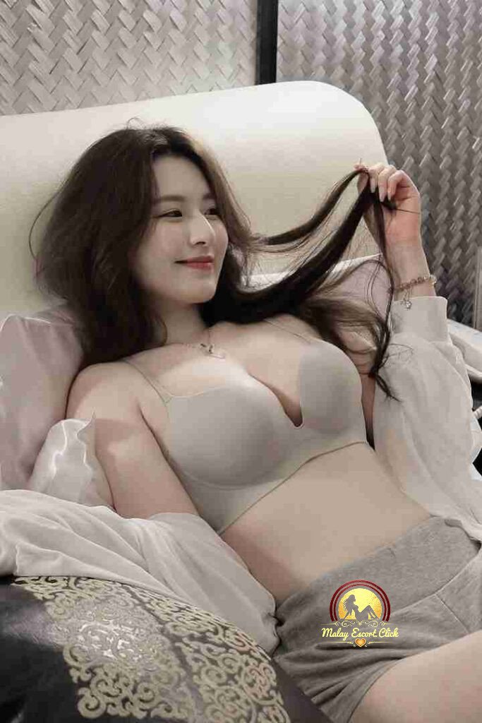 Attractive Asian woman in bra and shorts lounging on bed, smiling.