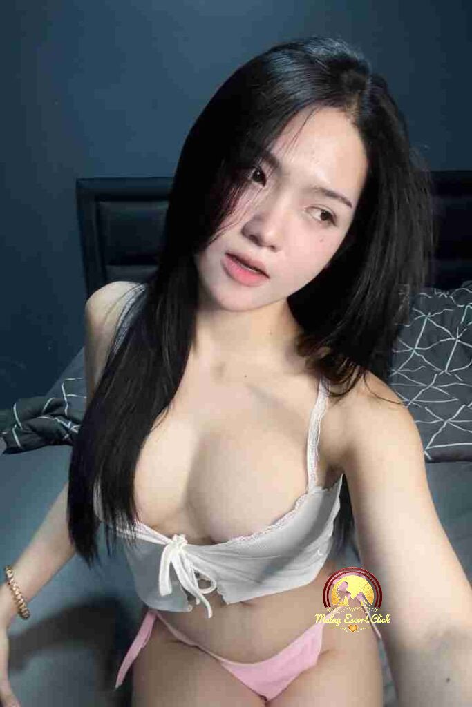 Malay Escort Girl Girl in black tube top lying on a green bed with messy hair and light makeup.