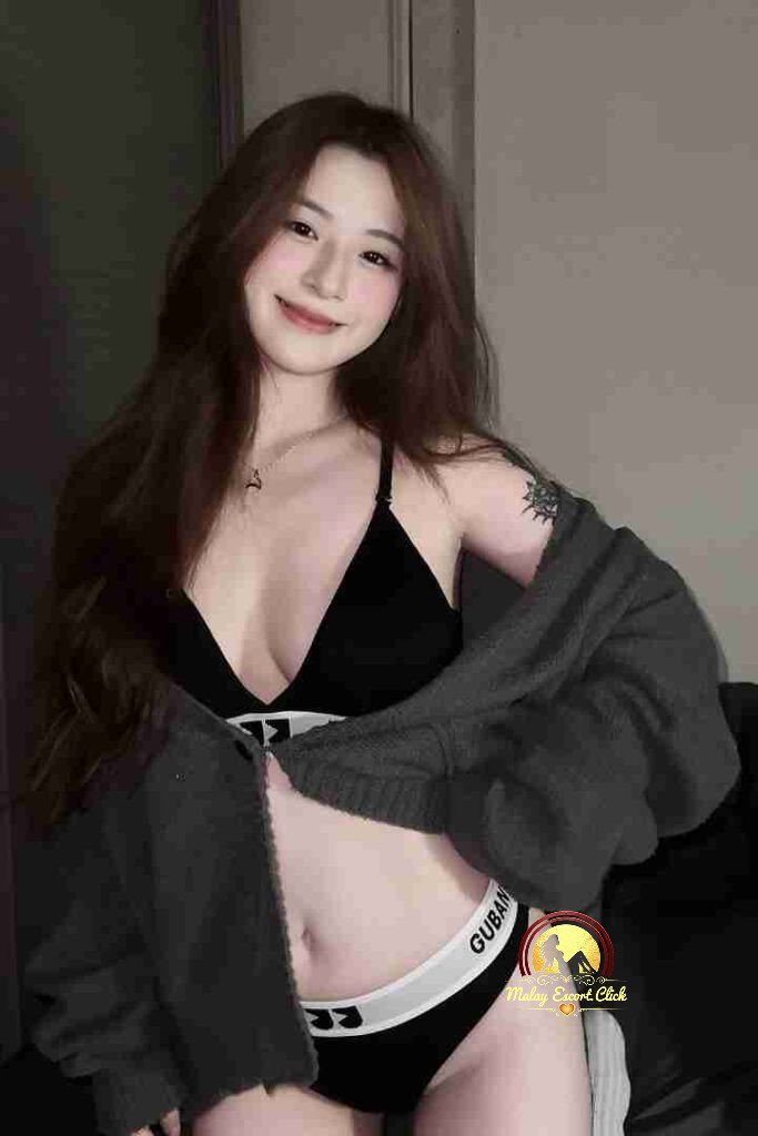 Smiling Asian woman in black lingerie and open cardigan, showing midriff. Kuala Lumpur escort.