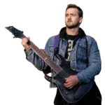 Man playing electric guitar with denim jacket and black shirt, purple strap.