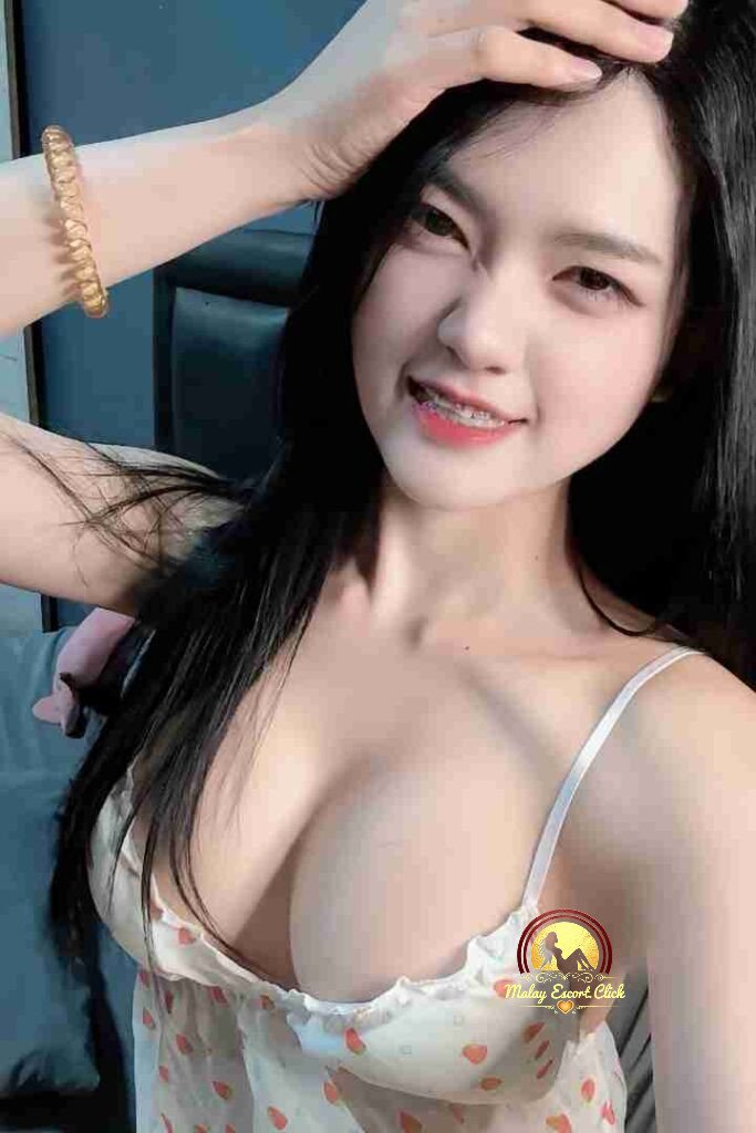 Malay Escort Girl Girl in black tube top lying on a green bed with messy hair and light makeup.