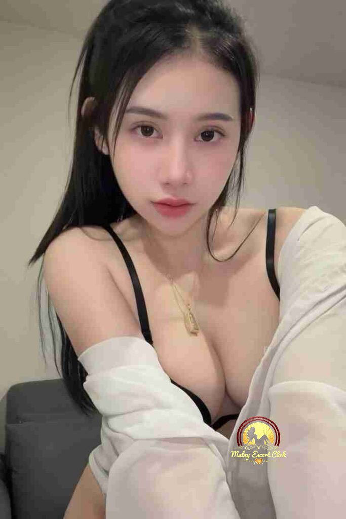 Malay Escort Girl Asian woman in a lacy top, posing near a cafe sign. Includes "Review us on Google, Free Brownie Cookie" text.