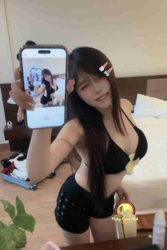 Smiling Vietnamese woman in black bikini holding phone with selfie. KL escort.