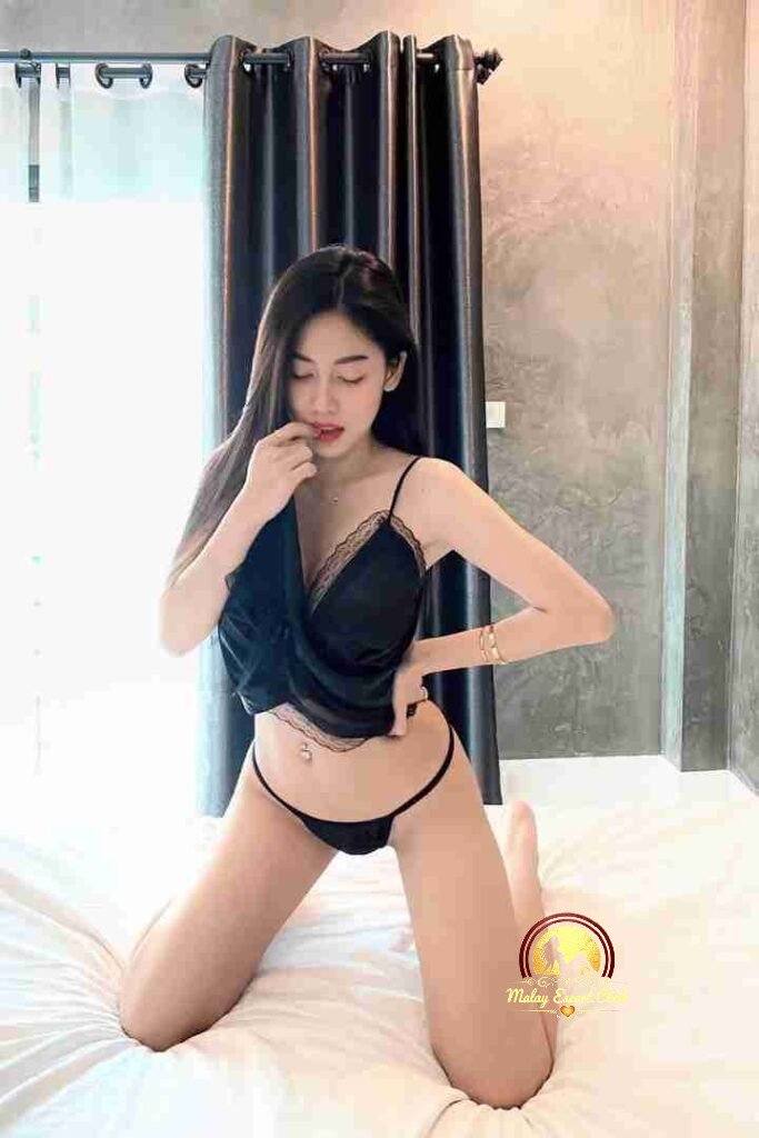 Malay Escort Girl Attractive woman in black top at outdoor cafe, holding phone. Evening ambiance.