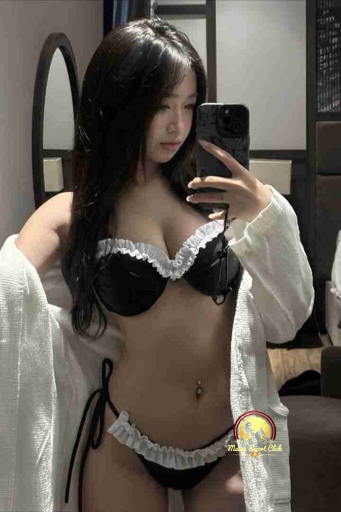 Woman in black and white lingerie taking a selfie in a bedroom with a white robe.