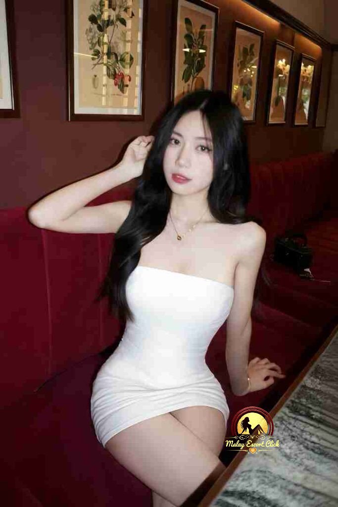 Beautiful woman in white dress on red couch. KL Escort.